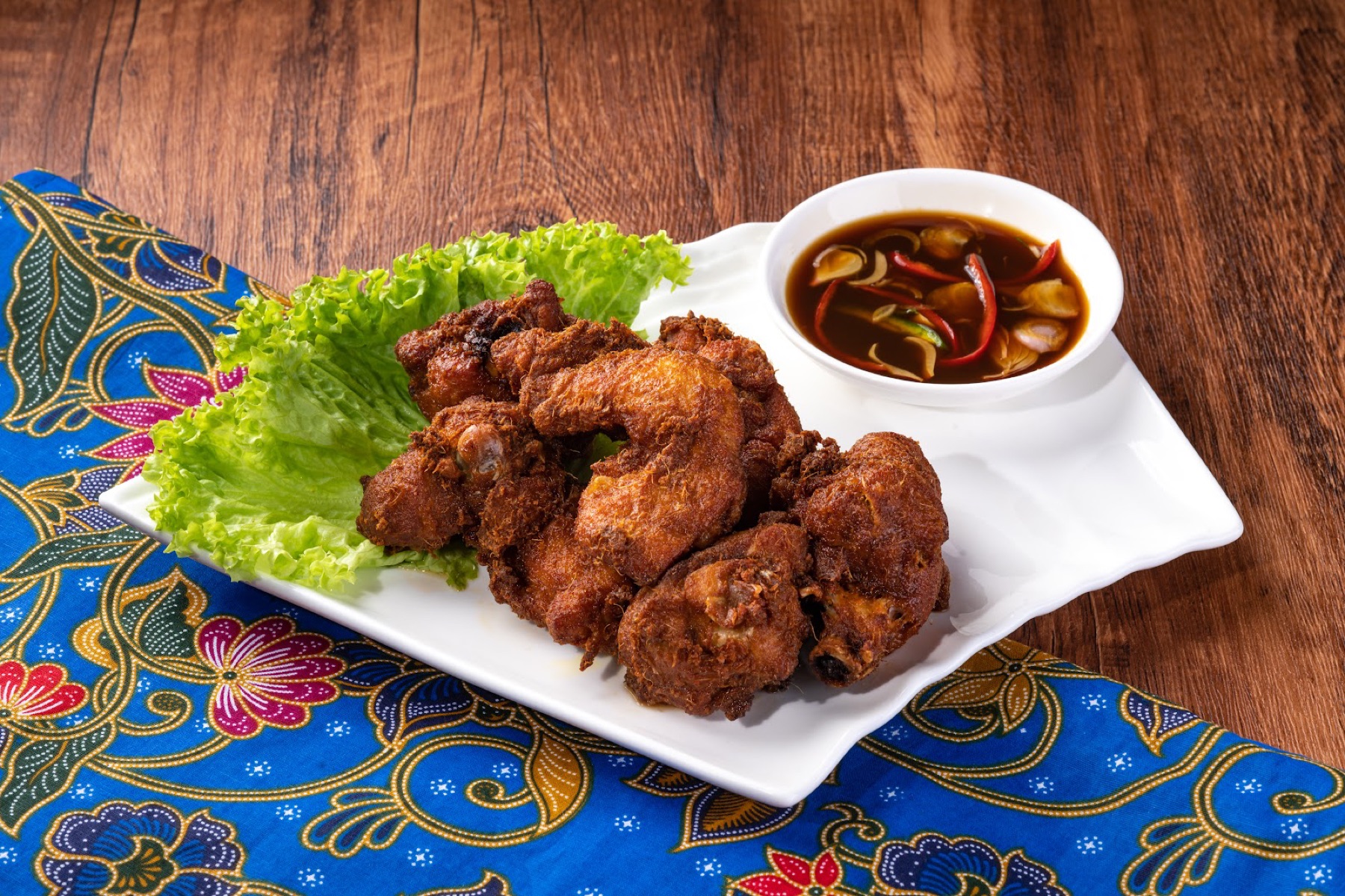 Golden fried Nyonya-style chicken with a tamarind-chilli dip, plated on a cobalt-blue Peranakan batik cloth