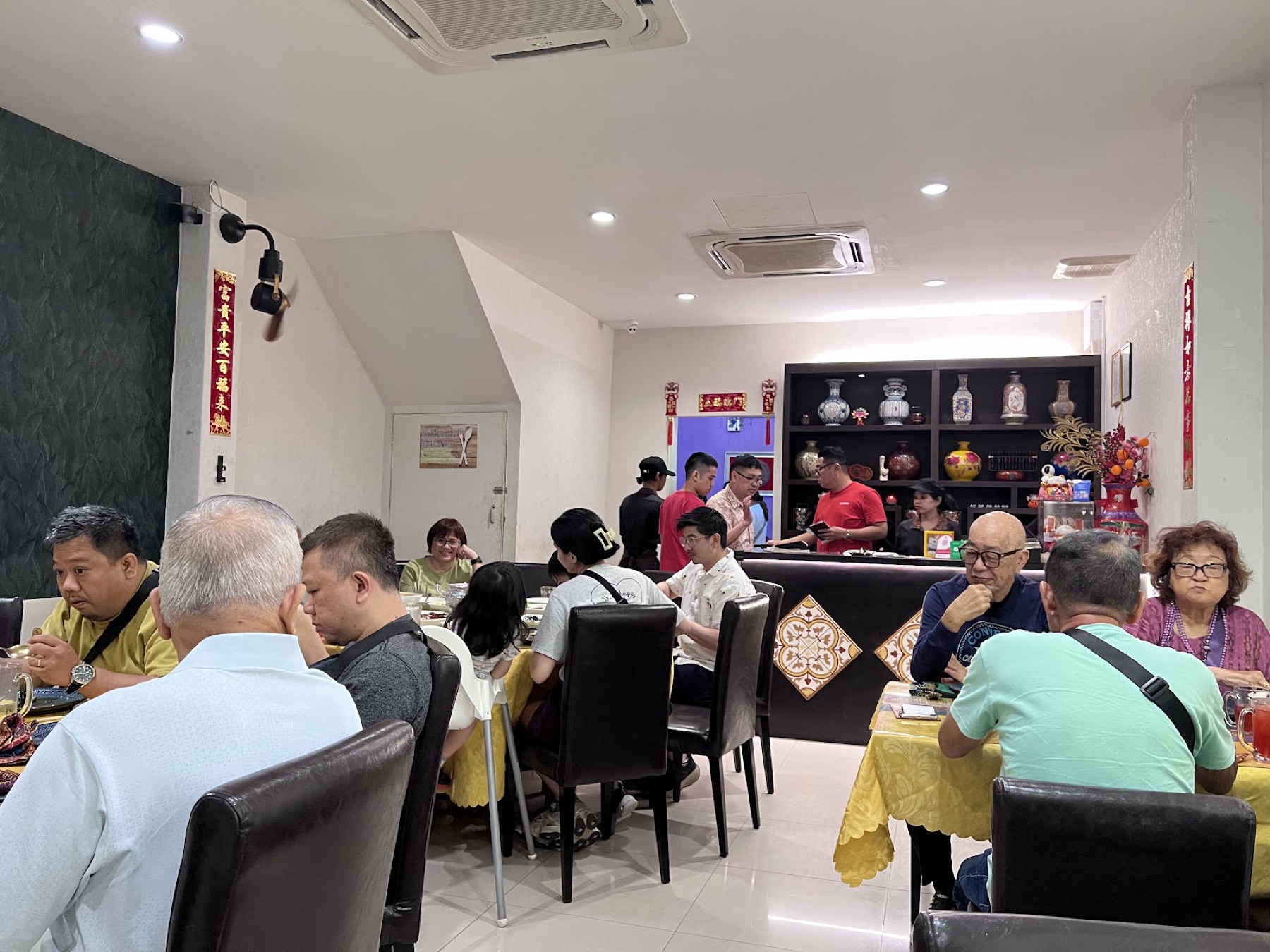 A busy dining room at Rasa Sayang — full tables, Chinese calligraphy couplets and a porcelain display cabinet